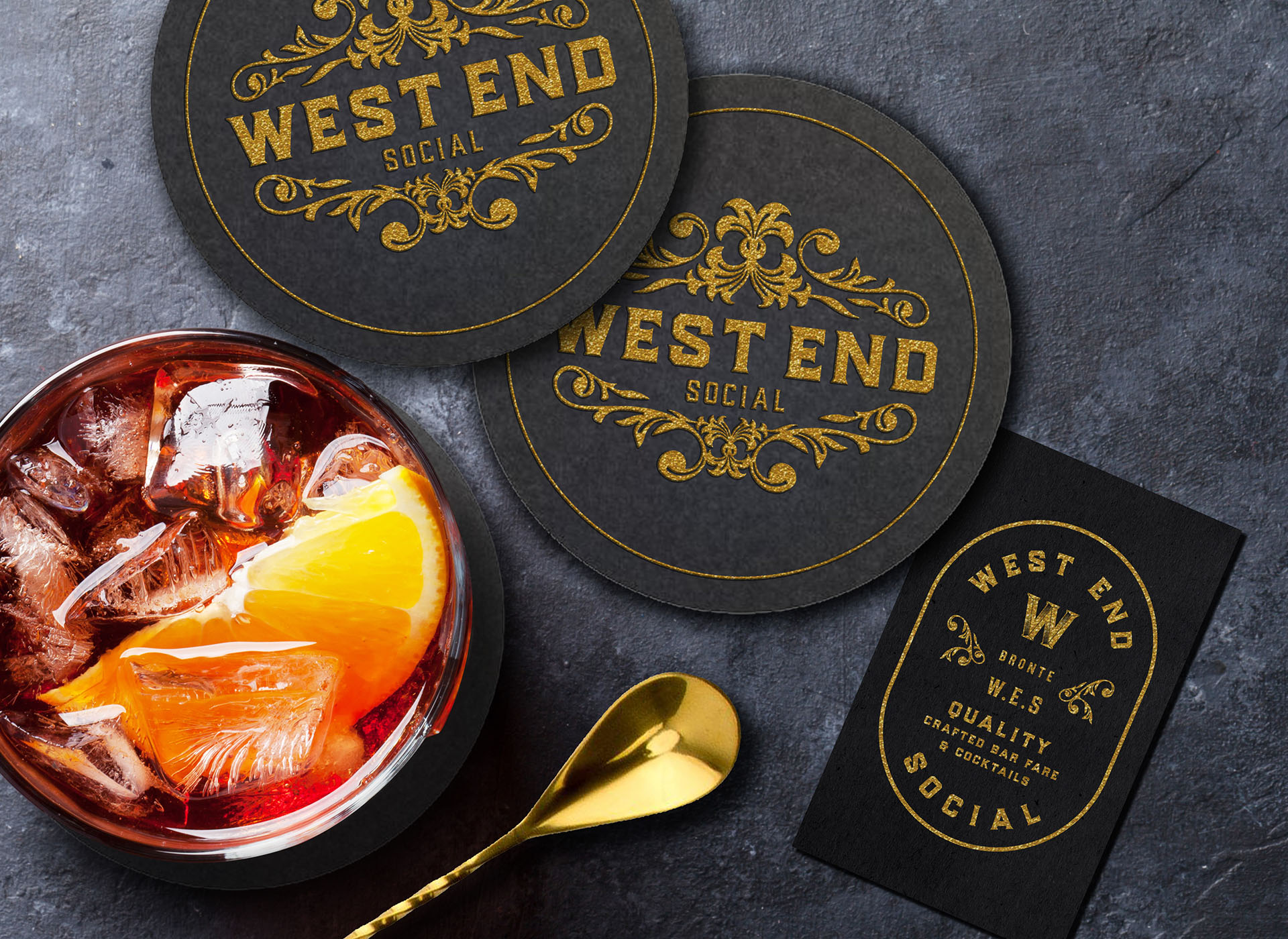 Cocktail, coasters, and business card for West End Social on to of a stone table